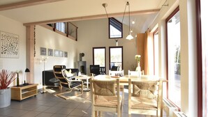 A spacious living area with a high ceiling, wooden beams, a fireplace, and large windows offering natural light. - Holiday House on the Island of Poel (Insel Poel)
