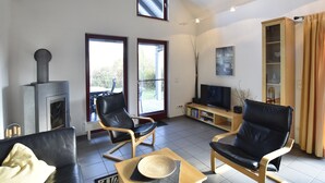 A modern living room with a fireplace, two black leather chairs, a wooden coffee table, and a television. - Holiday House on the Island of Poel (Insel Poel)
