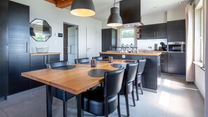 A modern kitchen with a wooden dining table and chairs, a large island, and built-in appliances.