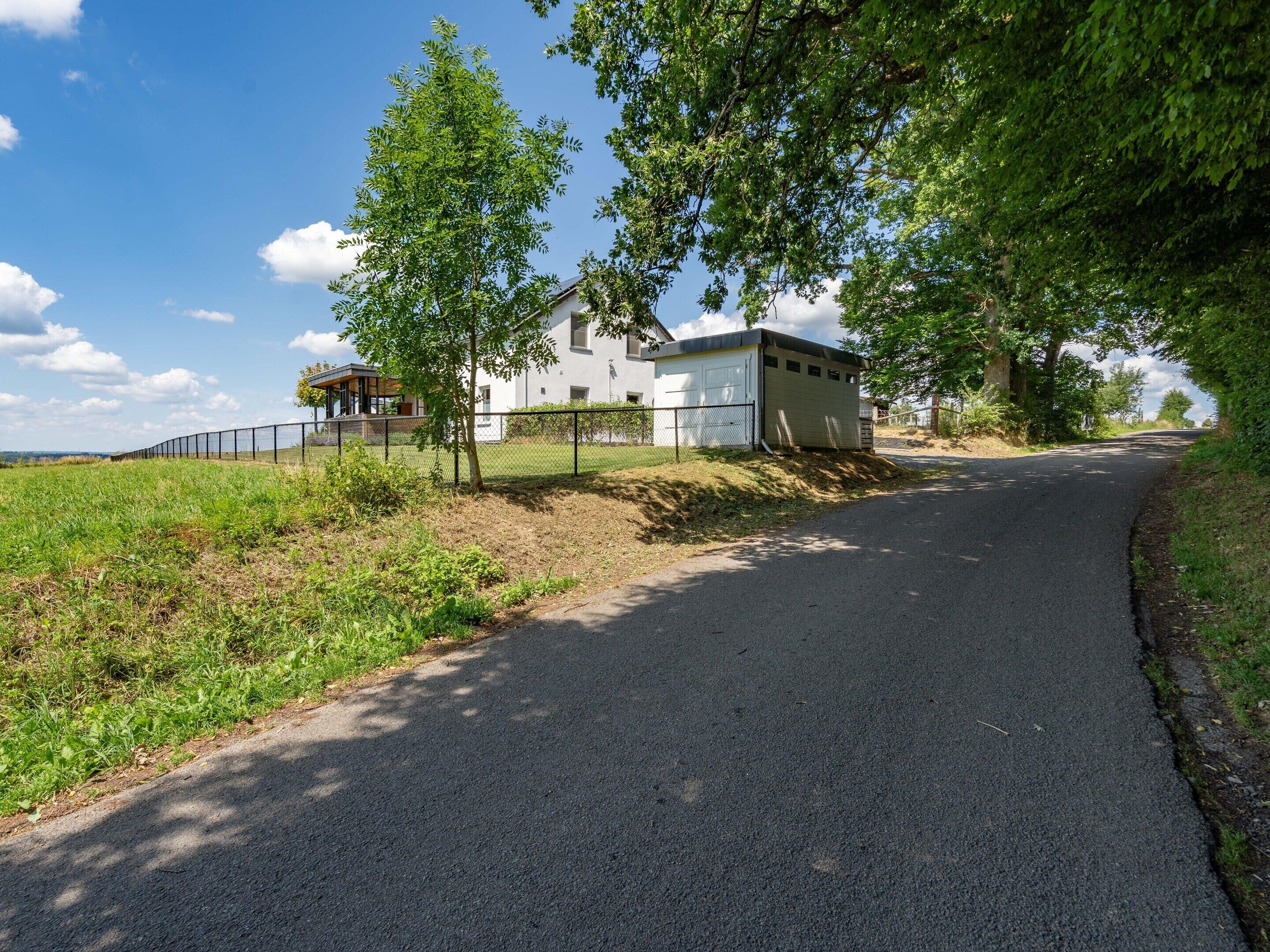 A rural road leading to a white house with a fenced yard and a garage.