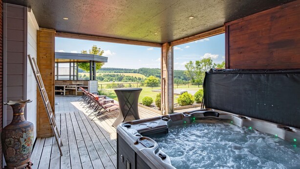 A hot tub on a wooden deck with a view of a mountainous landscape.