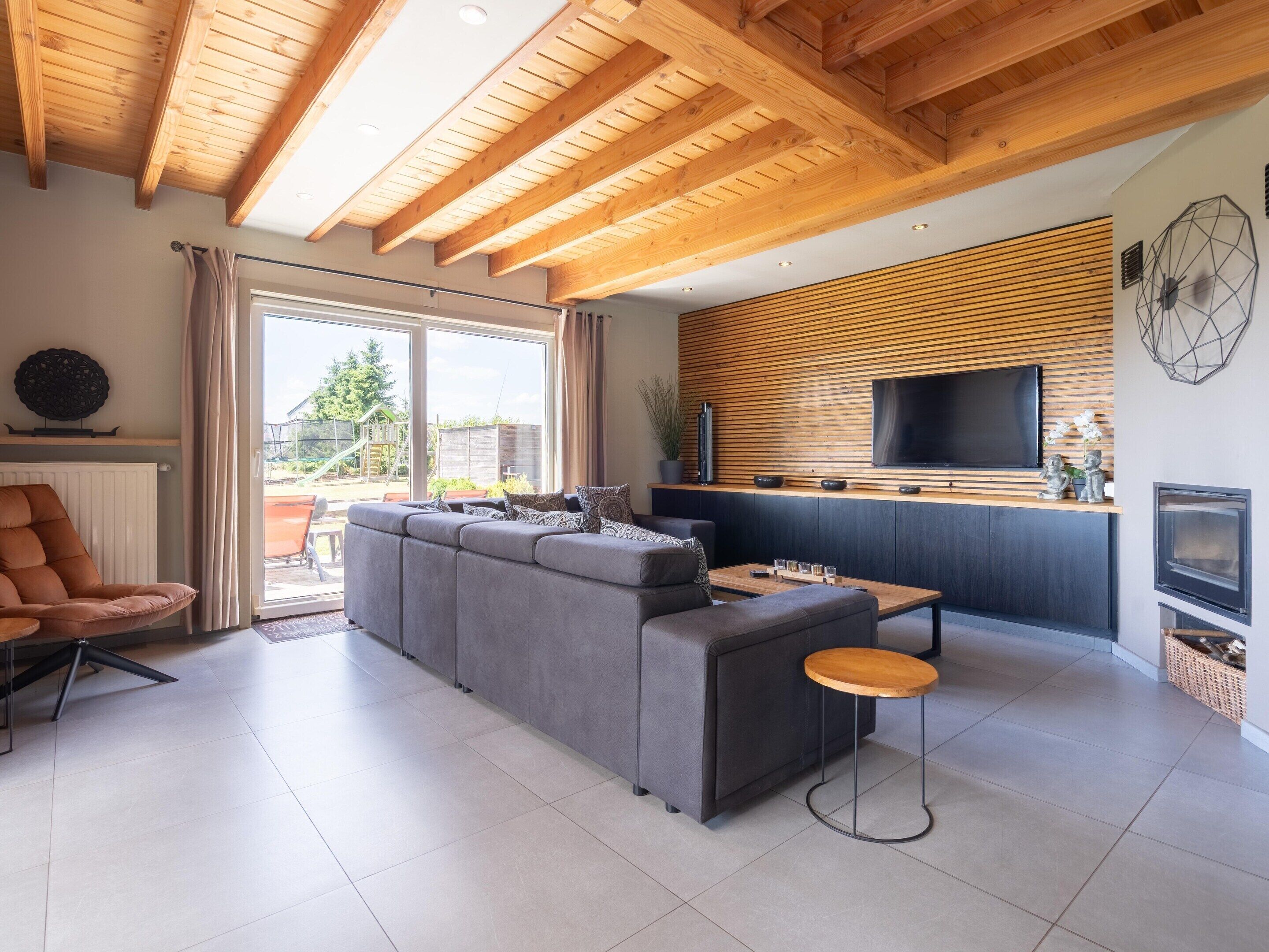 A modern living room with a sectional sofa, a wooden ceiling, and a TV mounted on the wall.