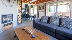 A modern living room with a wooden ceiling, a large sofa with patterned cushions, a coffee table, and a TV.