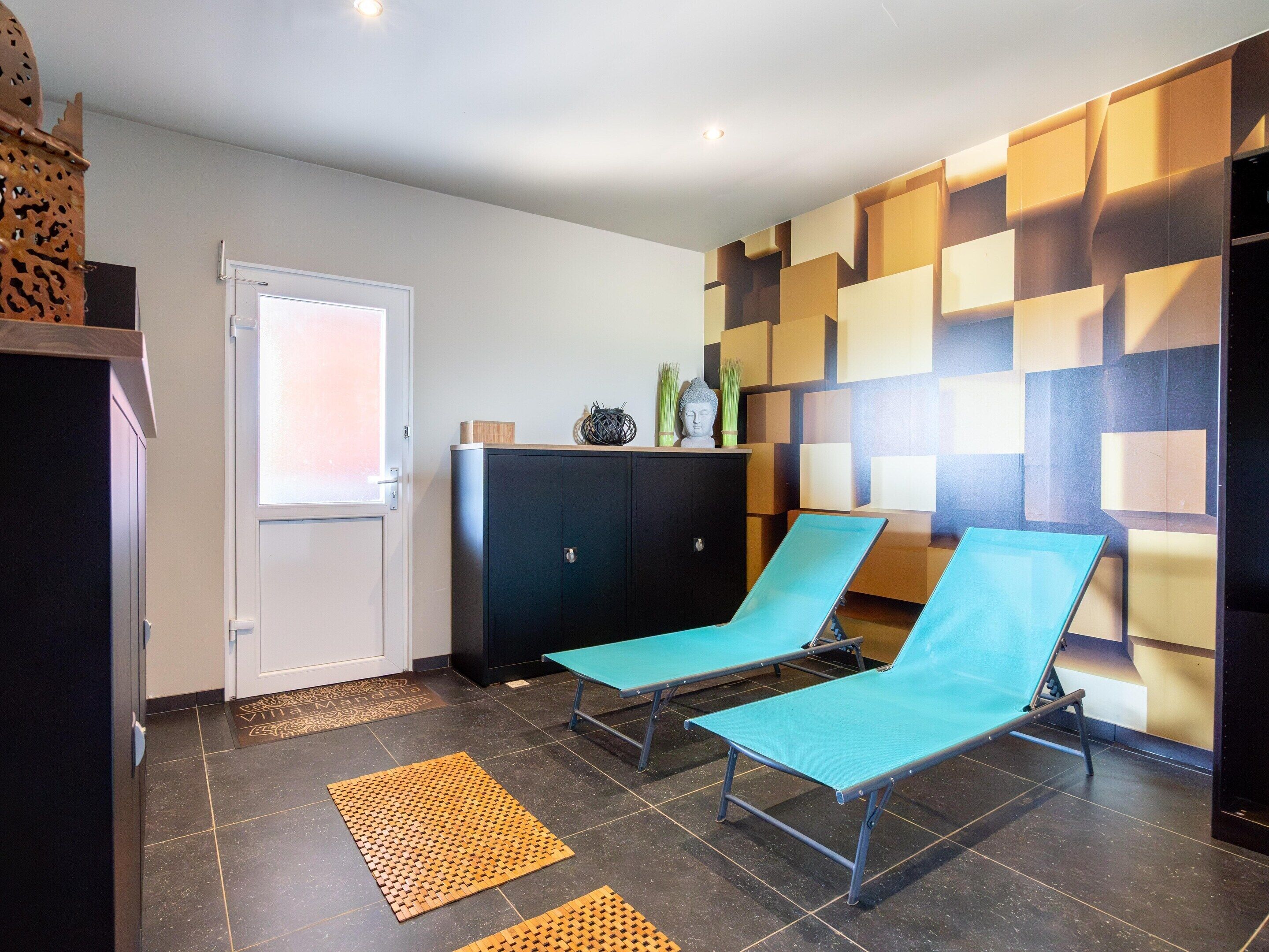 Ein Zimmer mit zwei blauen Lounge-Sesseln, einer schwarzen Kommode und einer Wand mit Muster.