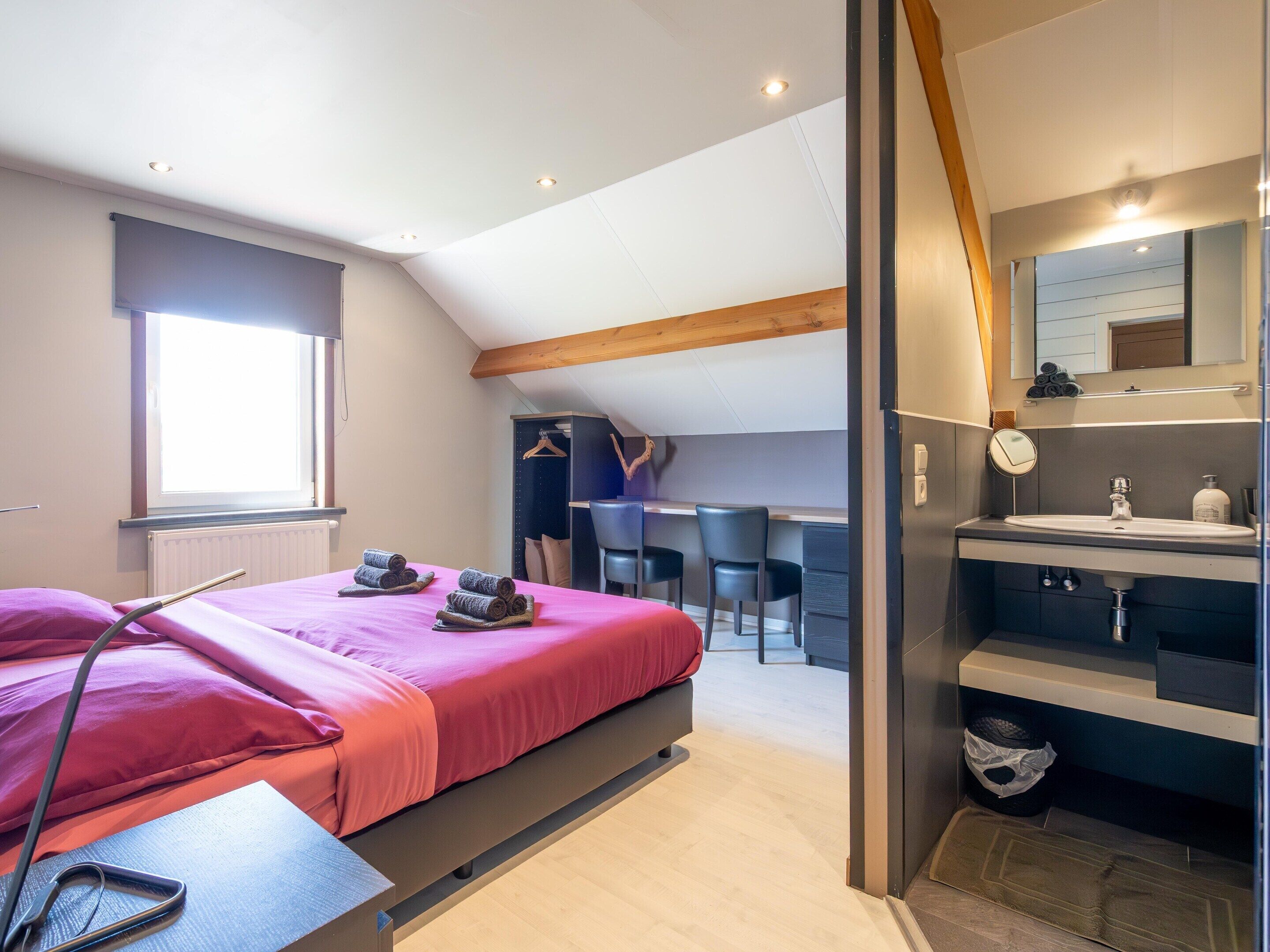 A bedroom with a bed, a desk, and a bathroom.