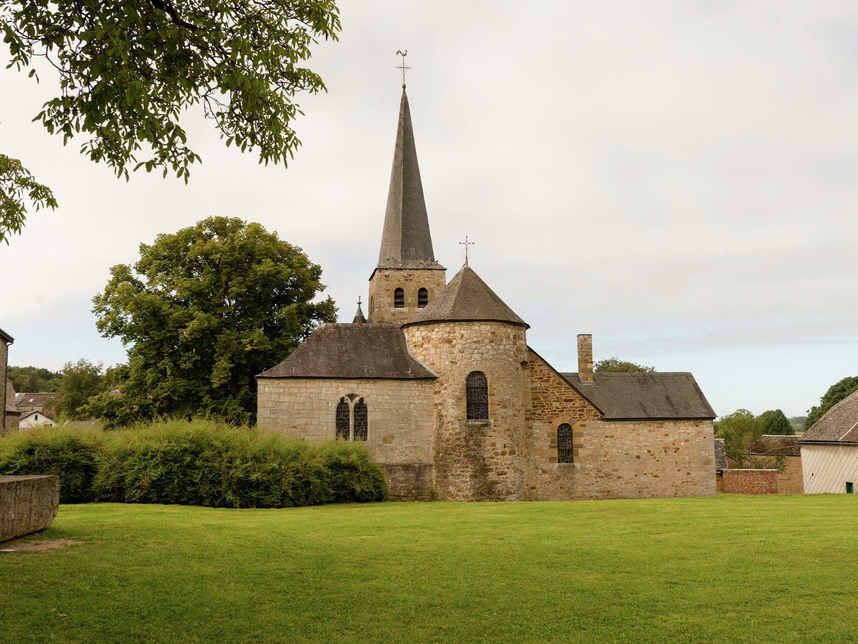 A church with a tall steeple, stone walls, and a grassy lawn.