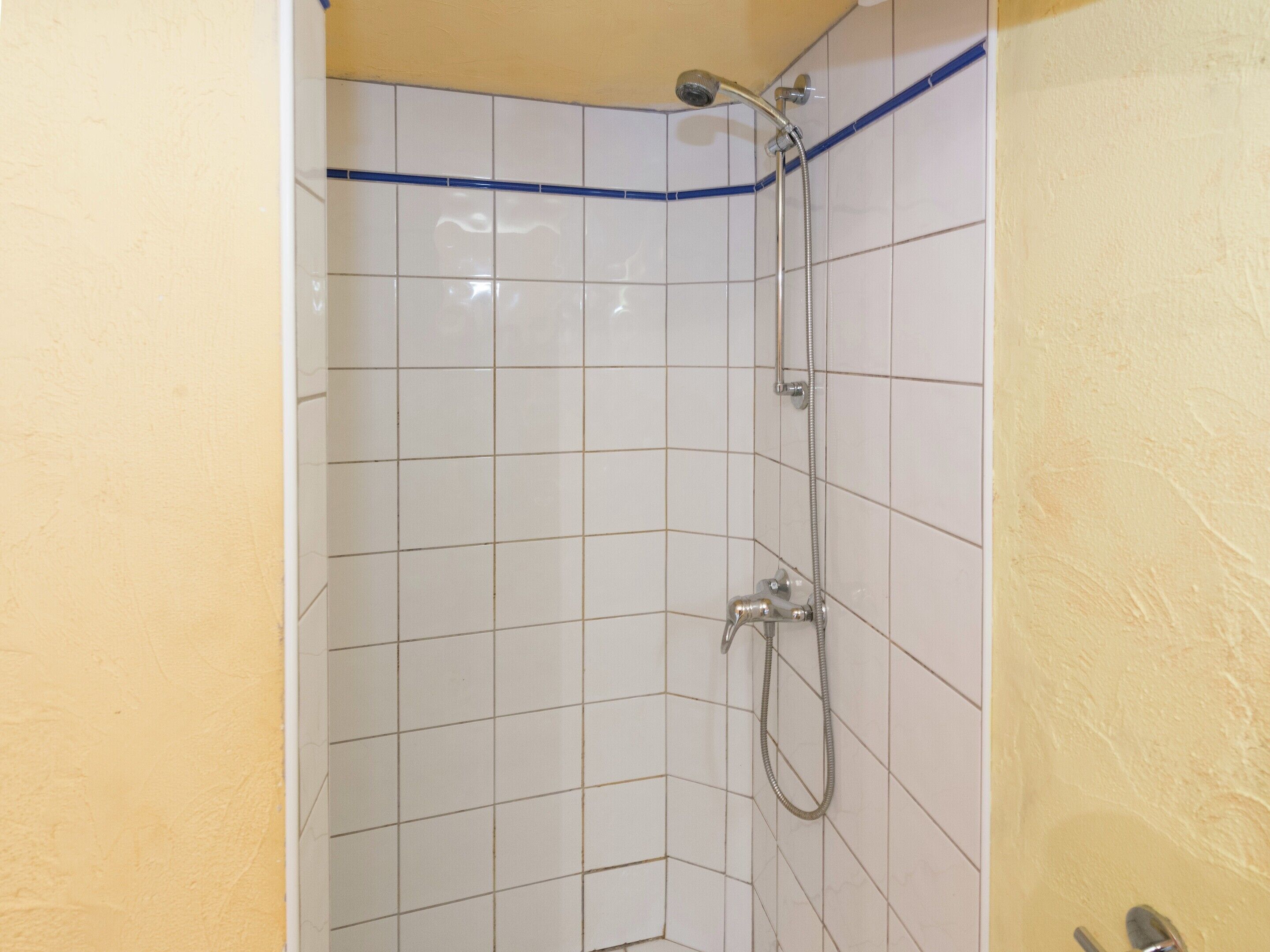 A small, tiled shower area with a handheld showerhead and a wall-mounted faucet.