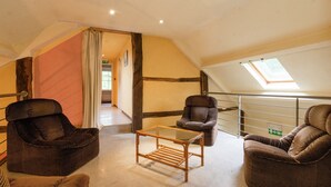 A loft-style room with a high ceiling, exposed beams, and a skylight. There are three wicker armchairs and a small wooden table. - Glorious Holiday Home in Wéris with Hot Tub (Durbuy)