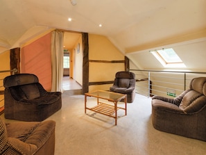 A loft-style room with a high ceiling, exposed beams, and a skylight. There are three wicker armchairs and a small wooden table.