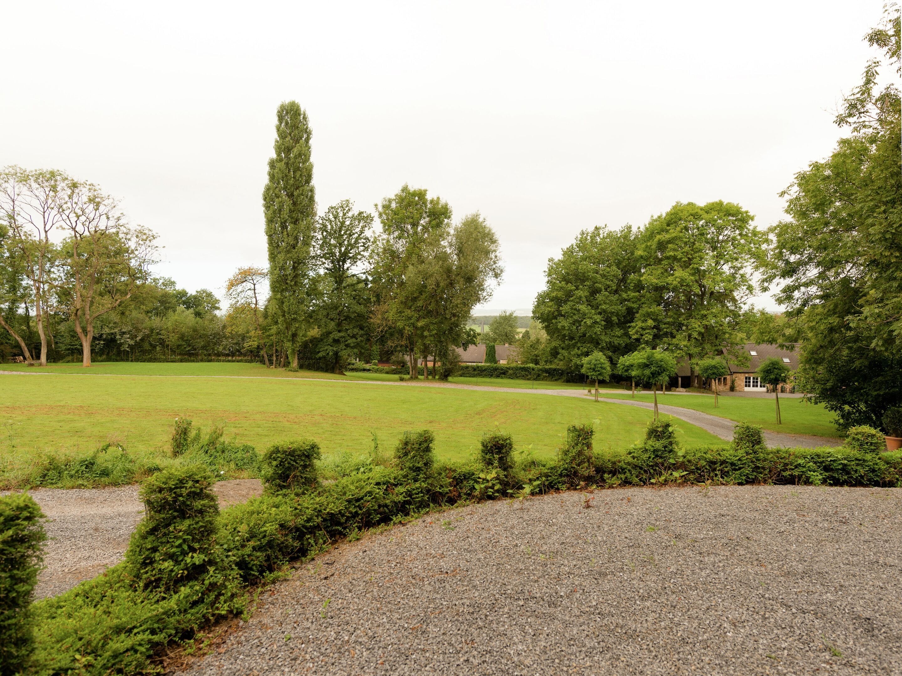 A grassy field with a gravel path, trees, and a building in the background.