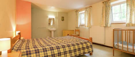 Un dormitorio con cama, una mesita de noche, cortinas en una ventana, un radiador y un espejo adosado a la pared.