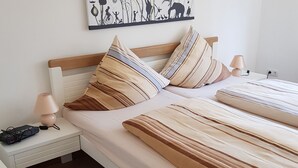 A neatly arranged bedroom with a wooden headboard, two pillows with striped patterns, a bedside lamp, and a power strip on the nightstand.