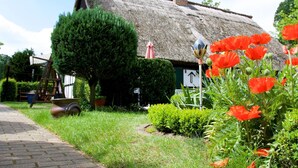 A traditional thatched-roof house with a well-maintained garden, including a hedge and poppies. - Sleep Under a Thatched Roof - Apartment in Ahlbeck near Haff (Ahlbeck)