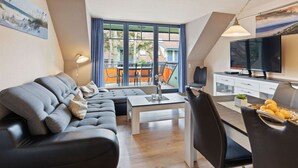 A modern living room with a sectional sofa, a dining table, and a TV. - Grosszugiges Apartment in Boltenhagen am Meer (Boltenhagen)