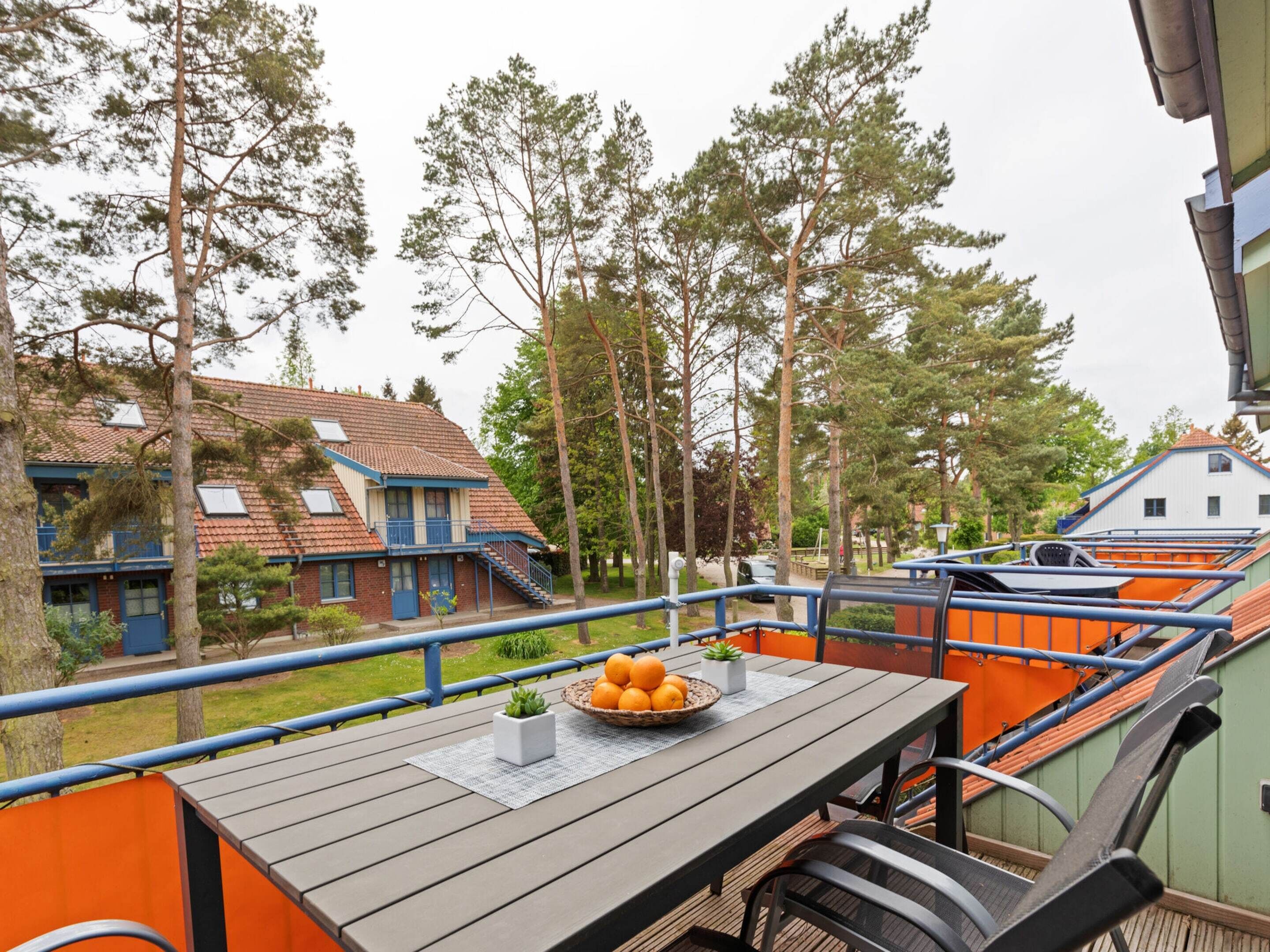 A wooden deck with a table set for dining, surrounded by orange railings and a view of residential buildings and trees.