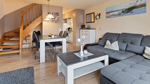 A modern living room with a grey sofa, a dining table, and a staircase. - Grosszugiges Apartment in Boltenhagen am Meer (Boltenhagen)
