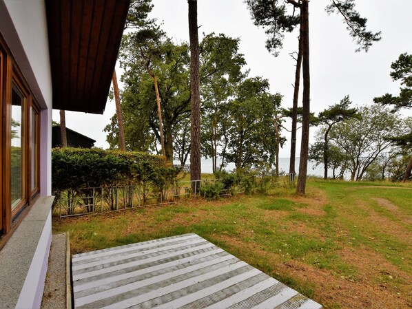 A wooden deck leading to a house with a view of a grassy area and tall trees.