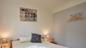A neatly made bed with a white comforter and pillows, a wooden headboard, a bedside table with a lamp, and a wall-mounted artwork. - Holiday Home in Am Salzhaff (Am Salzhaff)