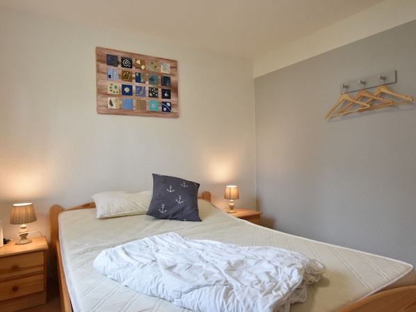 Ein ordentlich bezogenes Bett mit weißer Decke und Kissen, ein hölzernes Kopfteil, ein Nachttisch mit Lampe und ein an der Wand befestigtes Kunstwerk.