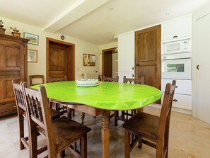 A dining room with a round table, wooden chairs, a green tablecloth, wooden cabinets, and a white oven. - Cozy Holiday House near La Roche (Rendeux)