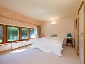A bedroom with a large window, a radiator, a bedside table with a lamp, and a bed with pillows. - Cozy Holiday House near La Roche (Rendeux)