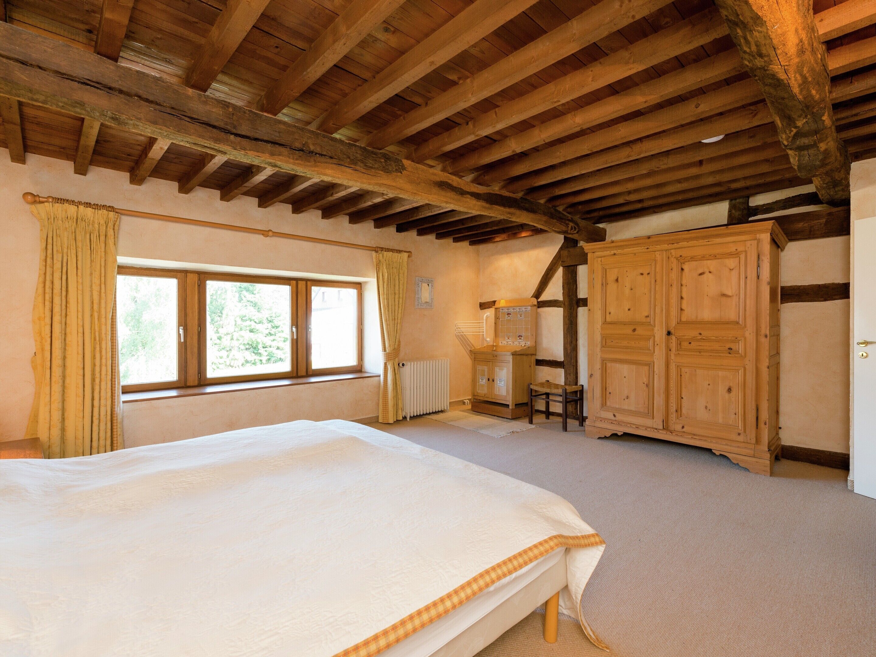 A bedroom with a large bed, wooden wardrobe, and a window with curtains.