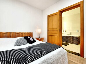A hotel room with a bed, a wooden headboard, a nightstand, a lamp, and a bathroom visible through an open door. - Countryside Escape for 9 (Beauraing)