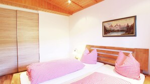 A bedroom with a wooden ceiling, a bed with checkered bedding, a painting on the wall, and a wooden wardrobe. - Chalet With Terrace in Niederndorf/kufstein (Niederndorferberg)