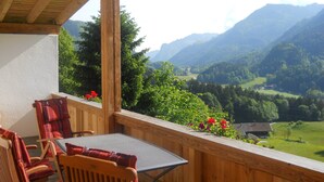 A wooden balcony with a table and chairs, overlooking a valley with mountains and greenery. - Chalet With Terrace in Niederndorf/kufstein (Niederndorferberg)
