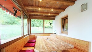 A wooden dining table with benches, large windows, and a view of greenery outside. - Chalet With Terrace in Niederndorf/kufstein (Niederndorferberg)