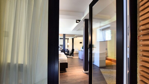 A modern hotel room with a large sliding glass door leading to a spacious living area. - Apartment in Former Coach House (Waimes)