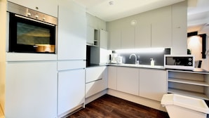 A modern kitchen with white cabinetry, a built-in oven, a microwave, and a coffee maker. - Apartment in Former Coach House (Waimes)