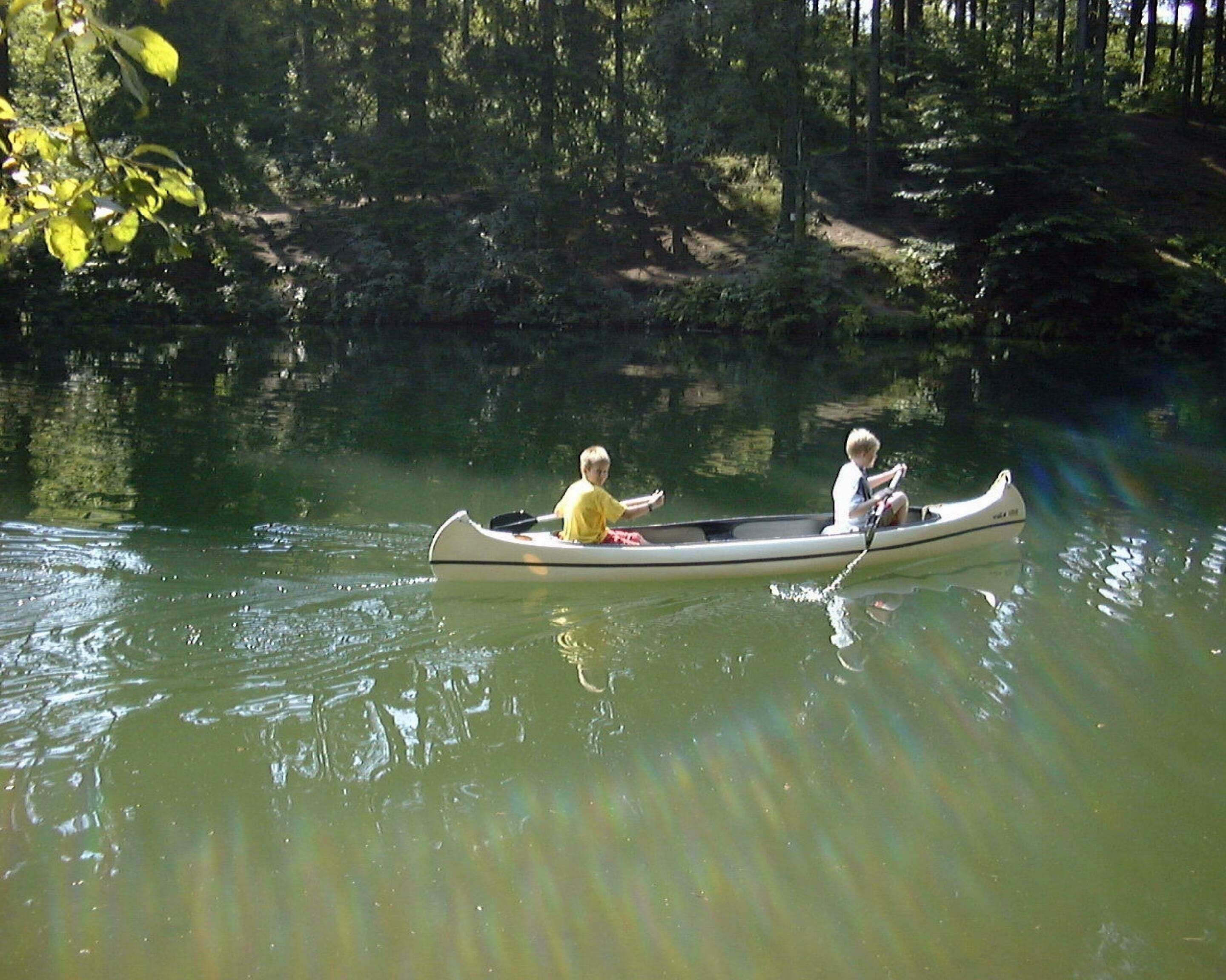 Ein Kanu auf einem ruhigen Fluss, umgeben von dichtem Wald.
