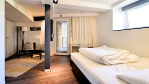 A modern hotel room with a bed, a desk, a chair, and a view of the outdoors. - Apartment in Former Coach House (Waimes)