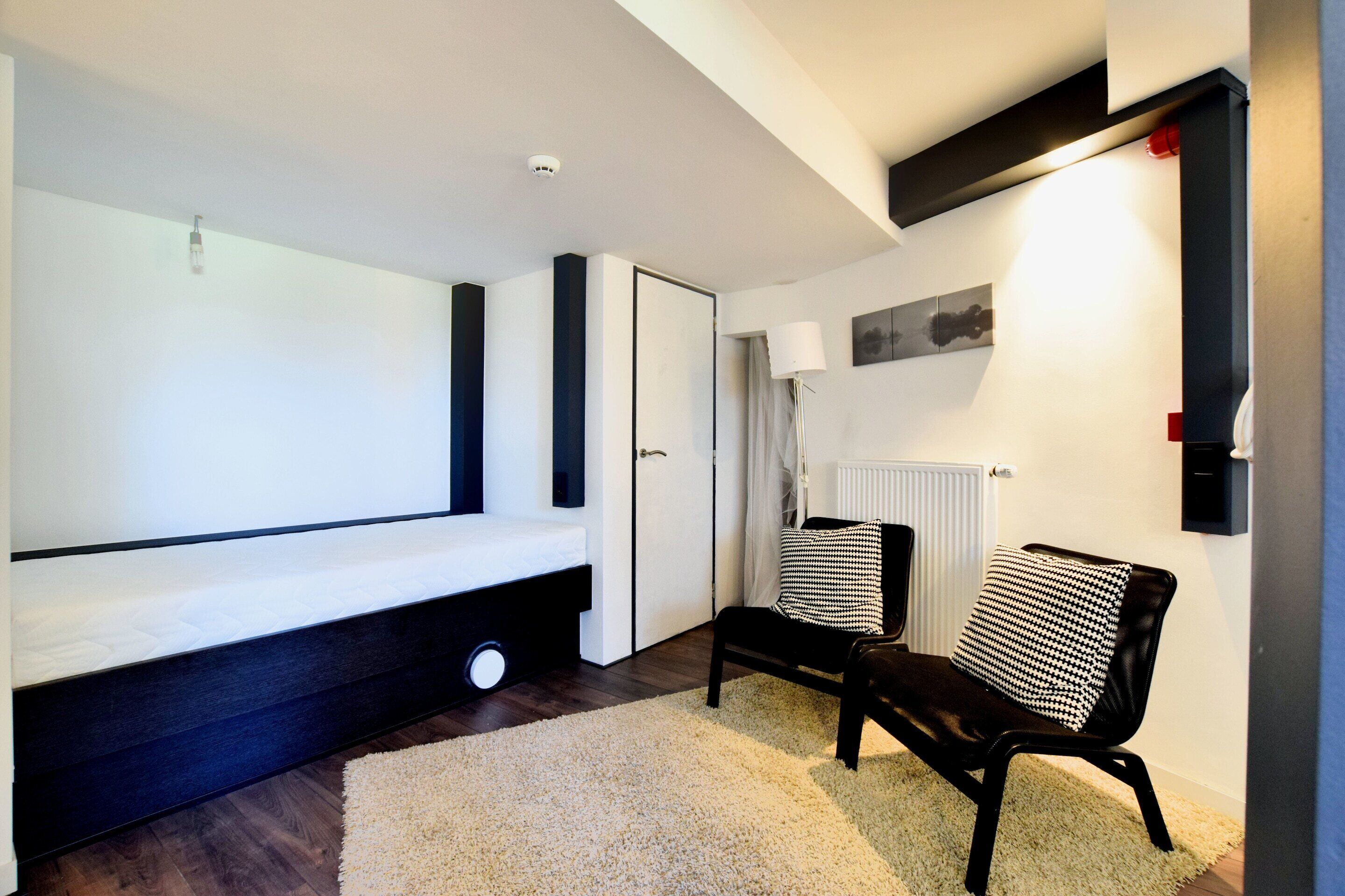 A modern room with a bed, a bench, a chair, and a radiator.