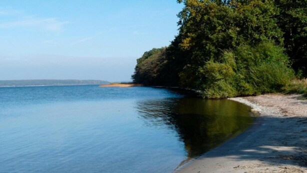 A calm lake with clear water, surrounded by trees and a sandy beach. - Quaint Holiday Home near Forest in Stuer (Stuer)