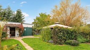 A green building with a covered porch, a stone pathway, and a variety of plants and trees. - Quaint Holiday Home near Forest in Stuer (Stuer)