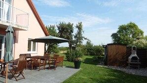 A patio with a table and chairs, a green umbrella, and a barbecue grill. - Pleasant Holiday Home in Malchow near Beach (Insel Poel)