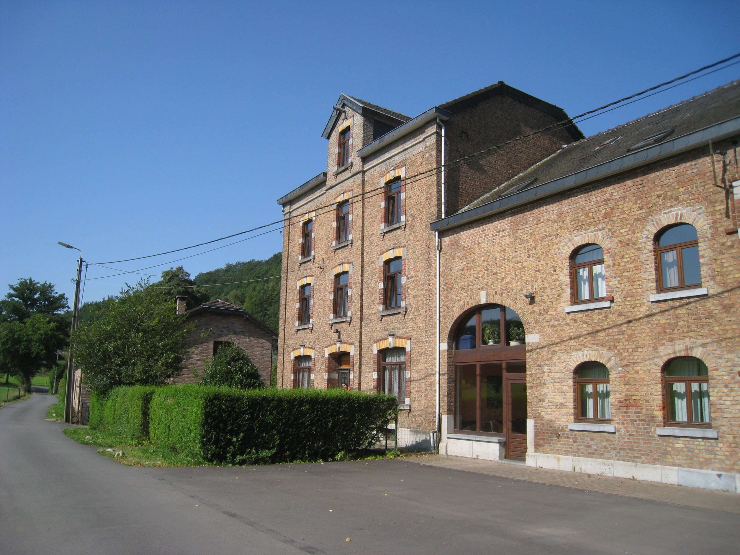 A two-story brick building with multiple windows, a large arched entrance, and a paved road in front.