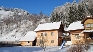 Un edificio de estilo chalé con techo cubierto de nieve, un telesilla y un cielo azul despejado.
