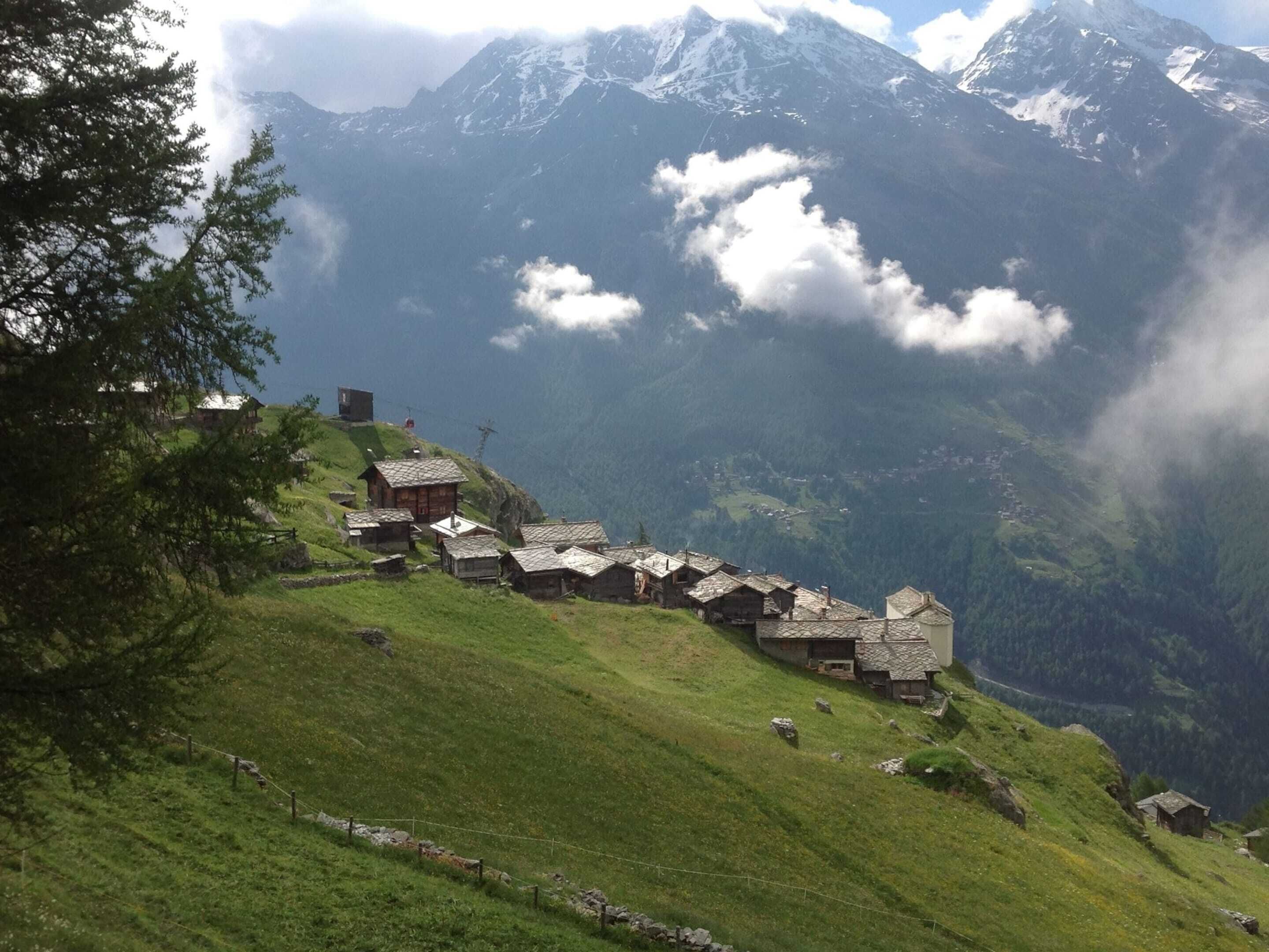 A cluster of traditional wooden houses on a hillside with a mountainous backdrop.