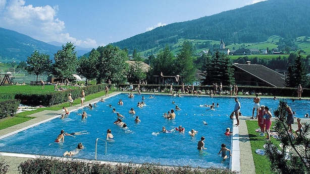 Una amplia piscina al aire libre rodeada de vegetación exuberante y montañas al fondo.