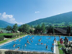 A large outdoor swimming pool surrounded by lush greenery and a mountainous backdrop. - Apartment in Rennweg Near Katschberg Ski Area (Rennweg am Katschberg)