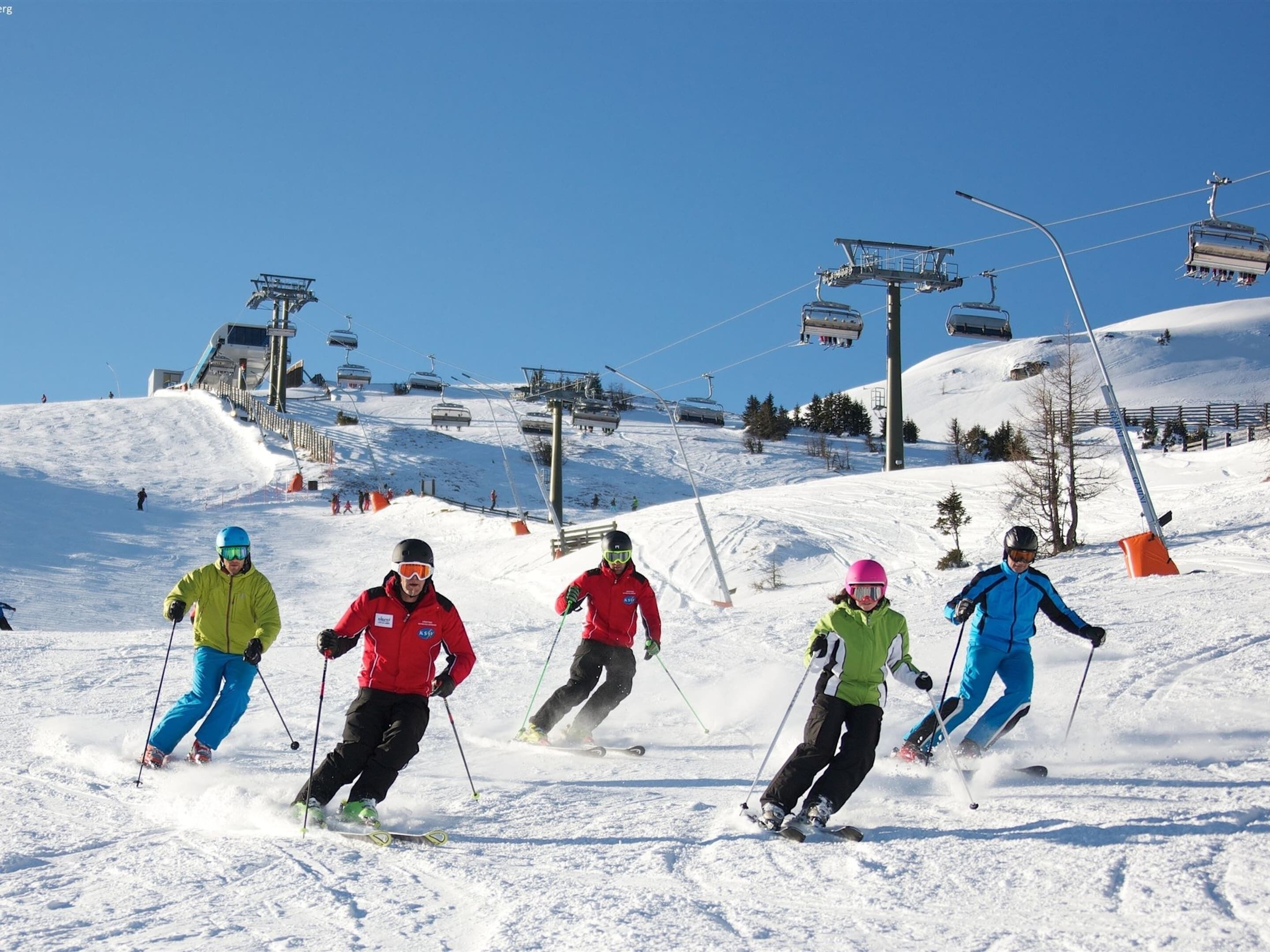 Eine Skipiste mit Skifahrern in Bewegung, Seilbahnen und blauem Himmel.