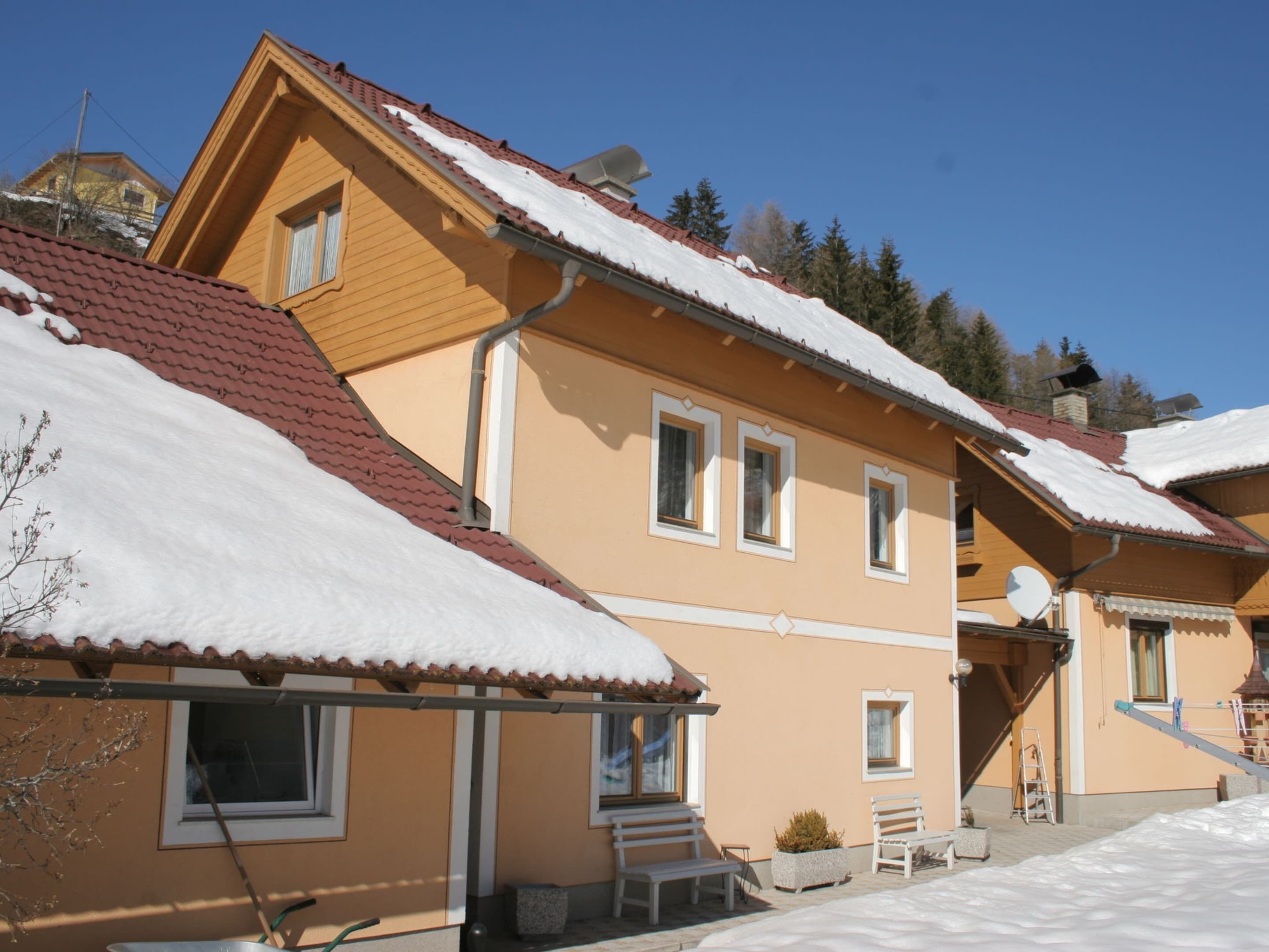 A two-story building with a sloped roof covered in snow, a balcony, and a small outdoor seating area.