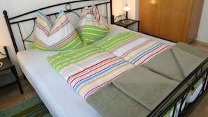 Una cama con ropa de cama a rayas coloridas, una mesita de noche con una lámpara y un armario de madera.