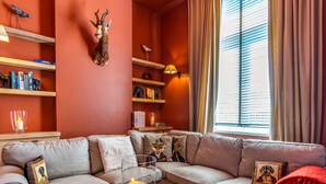 A cozy living room with a sectional sofa, a coffee table with a candle, and a wall-mounted deer head. Shelves with books and decorative items are visible. - Villa in Former School (Heers)