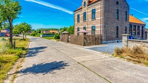 A two-story brick building with a red-tiled roof, a paved driveway, and a clear blue sky. - Villa in Former School (Heers)