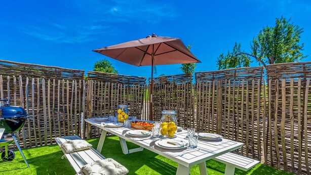 An outdoor patio with a table set for dining, a grill, and a wooden fence. - Villa in Former School (Heers)