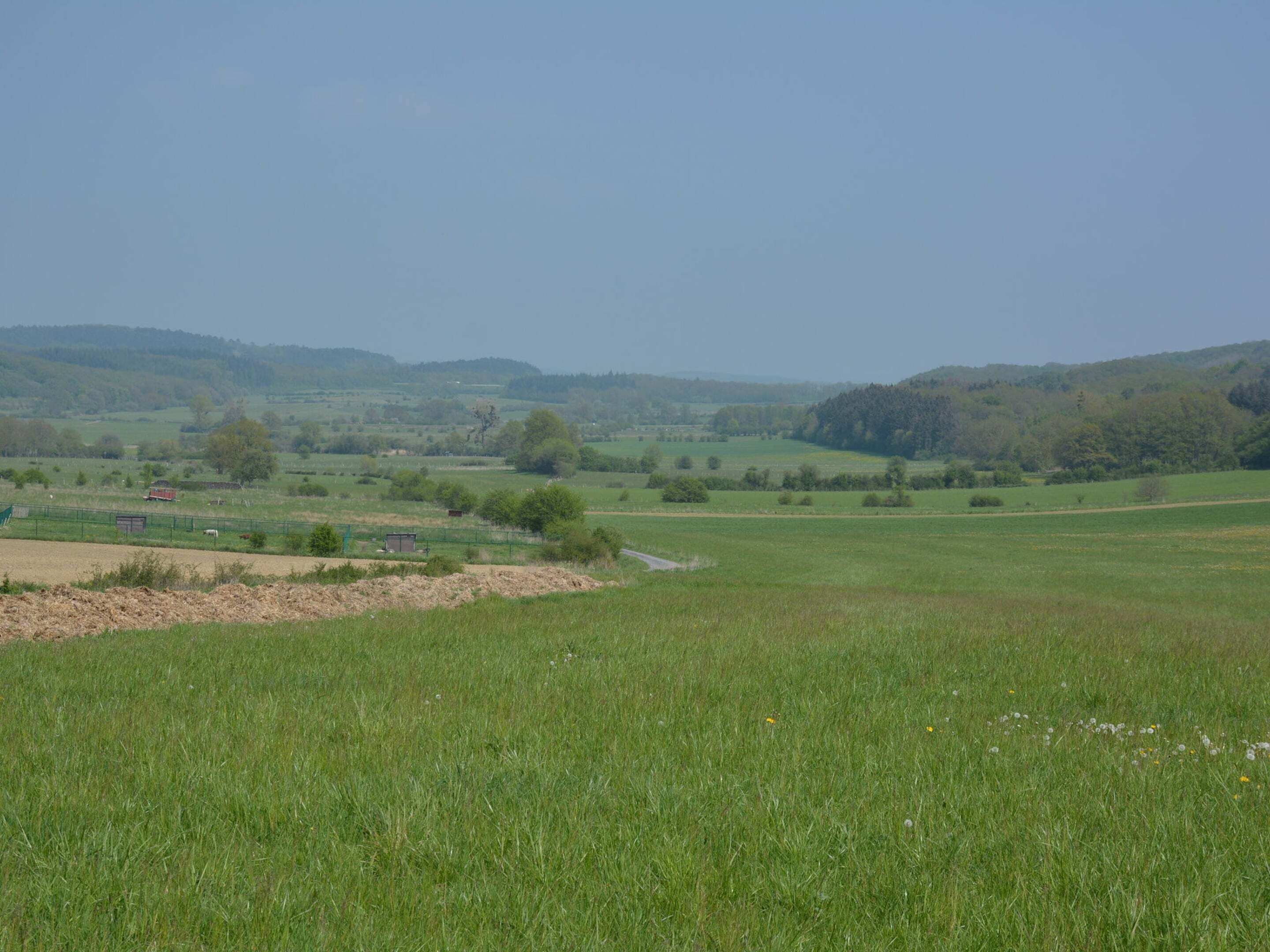 A rural landscape with open fields, a few scattered buildings, and rolling hills in the background.
